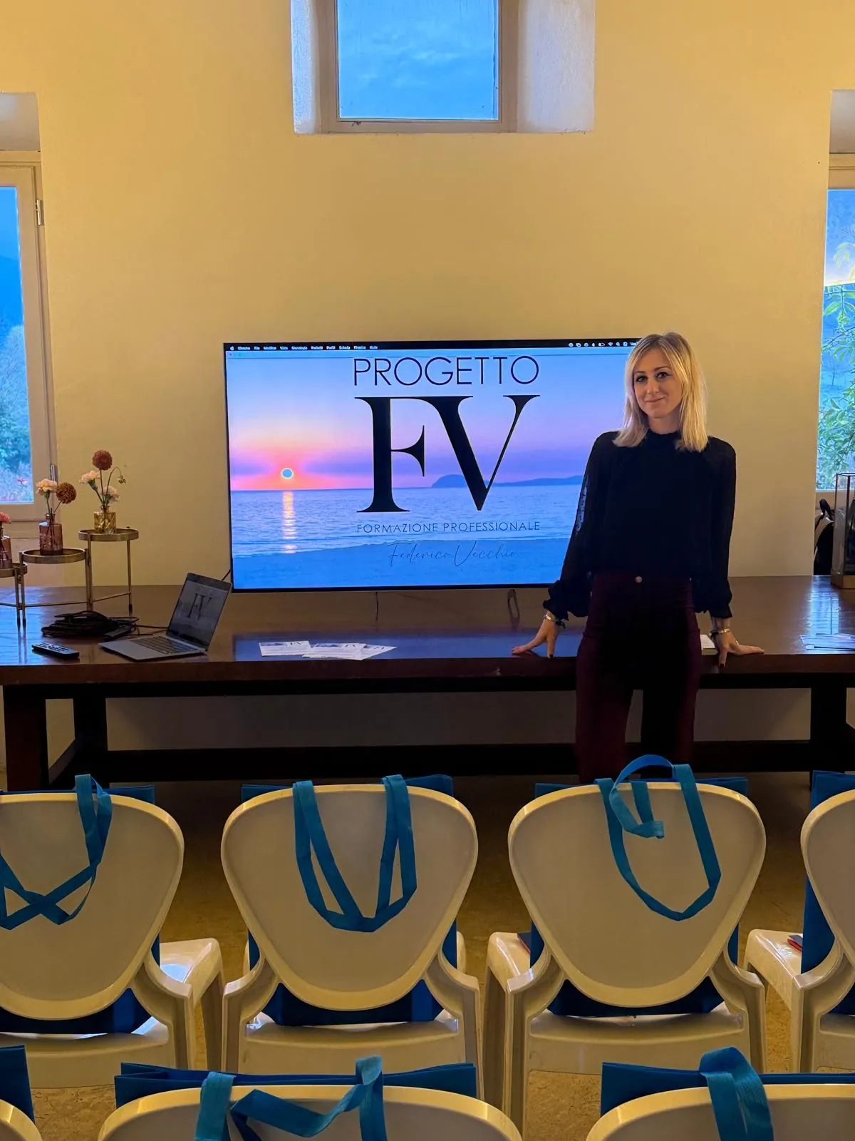 Ameni Ajam in sala prima dell'inizio di un evento, davanti allo schermo con il logo Progetto FV